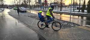 Zdjęcie przedstawia rowerzystę z dzieckiem podczas jazdy po ścieżce rowerowej