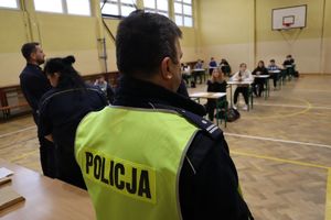 Zdjęcie przedstawia policjanta ubranego w kamizelkę z napisem Policja podczas części teoretycznej turnieju na sali gimnastycznej